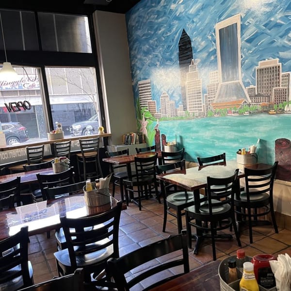 Interior of Gili's Kitchen with tables, chairs, and a mural of a city skyline over water.