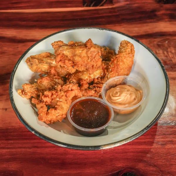 Crispy fried chicken pieces with two dipping sauces, one dark and one light, on a white plate.