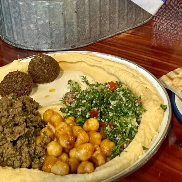 A large platter of Gili's Kitchen hummus topped with falafel, ground meat, chickpeas, and tabbouleh.
