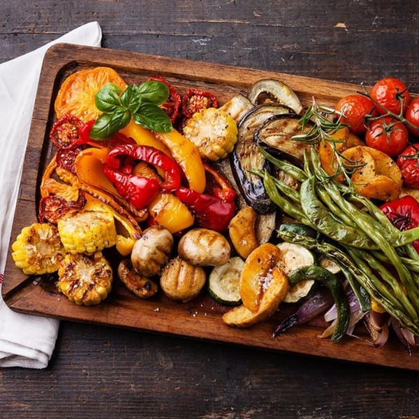 A wooden board filled with a colorful assortment of grilled vegetables, including corn, peppers, and tomatoes.