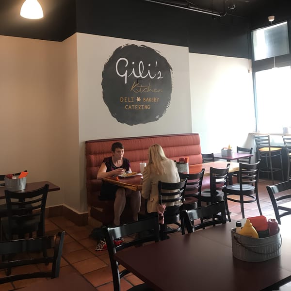 Two women dining at a booth in Gili's Kitchen, with tables and chairs filling the restaurant.